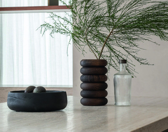 Home & Trends interieurselectie: Decoratieve vazen en objecten in donkere aardetinten op een lichte tafel.